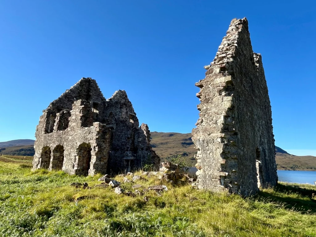 Die freistehenden Giebelwände der Calda House Ruine in einer grünen Graslandschaft am Ufer des Loch Assynt in Schottland.