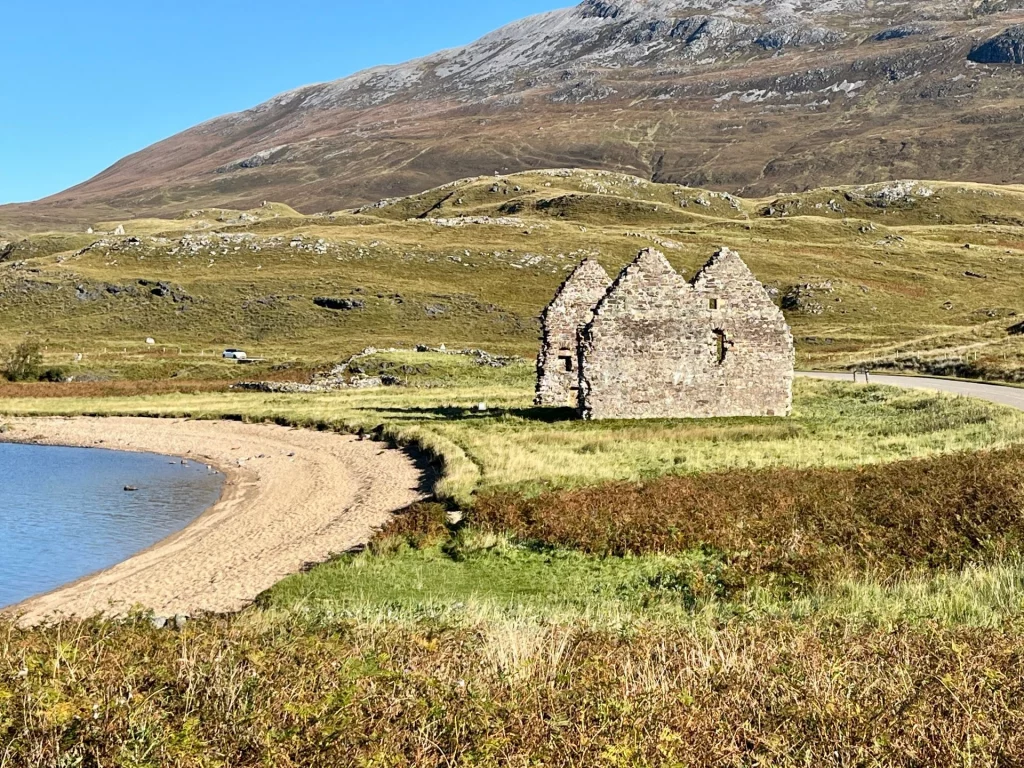 Historische Steinruine des Calda House in einer weiten Graslandschaft am sandigen Ufer des Loch Assynt in den schottischen Highlands.