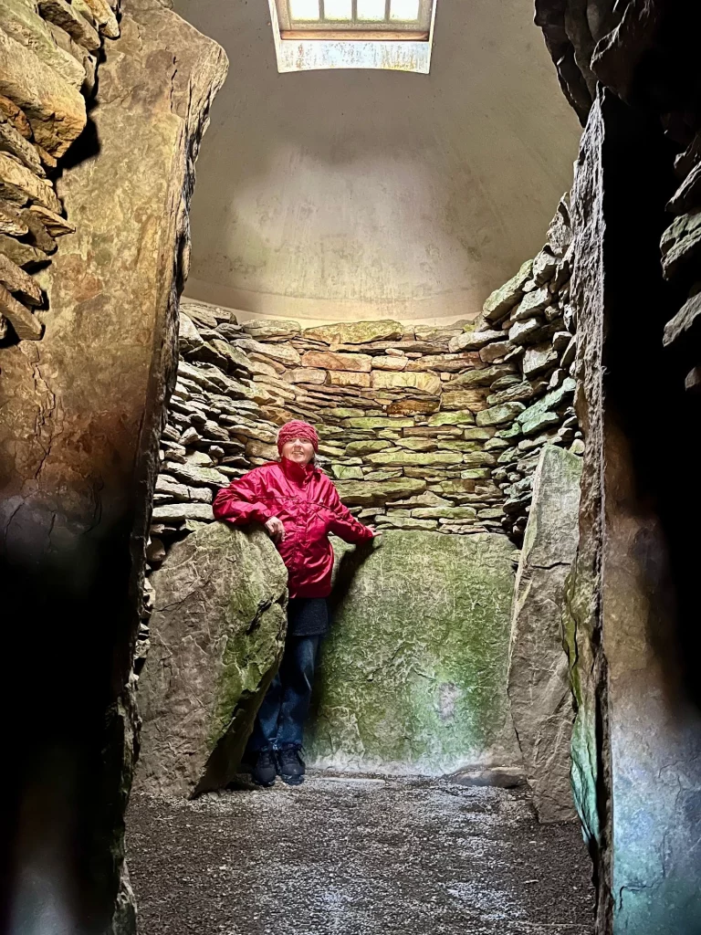 Eine Person steht in einer hohen, runden Steinkammer mit einer modernen Lichtkuppel an der Decke und massiven vertikalen Steinplatten am Boden.