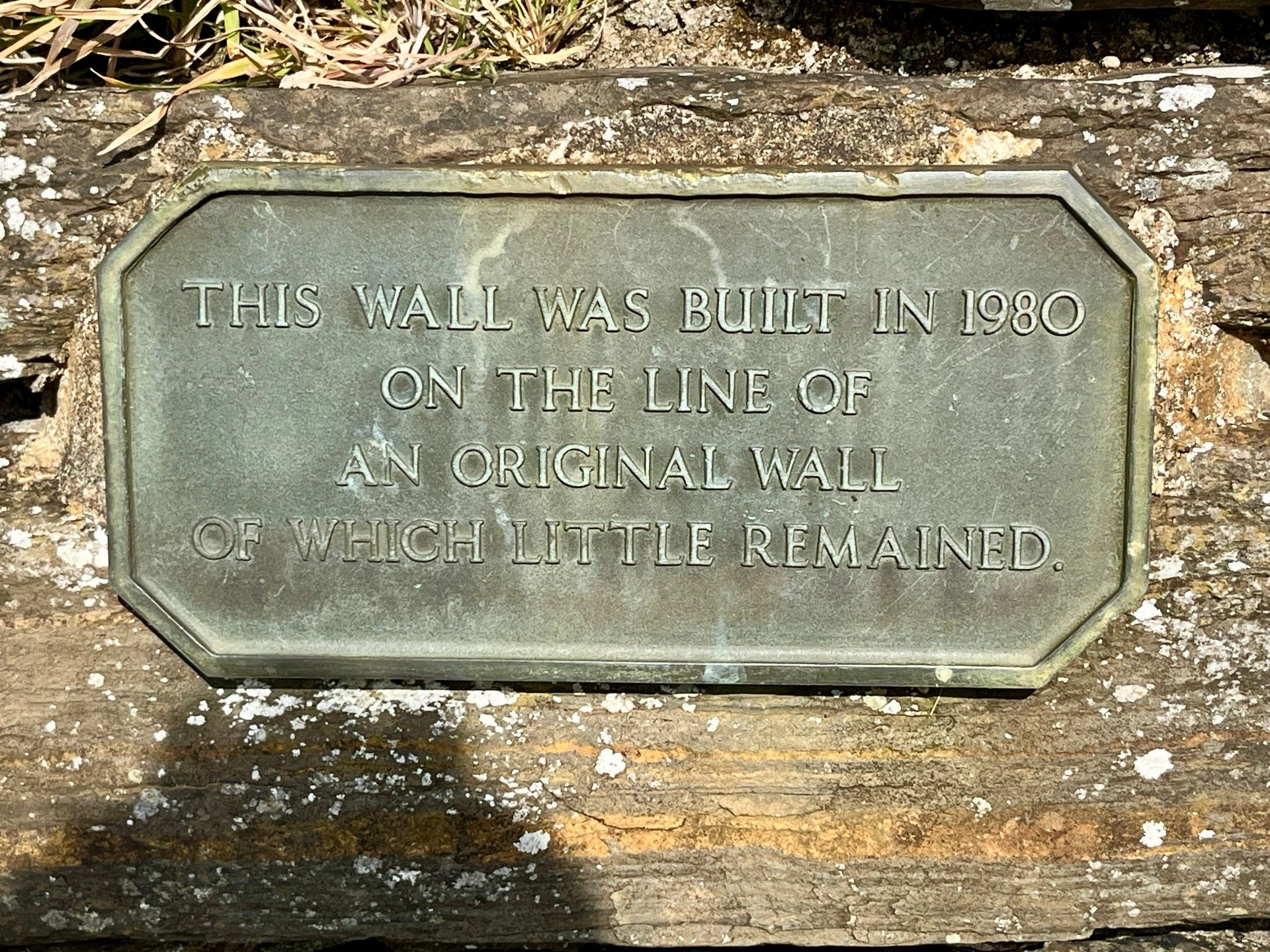 Eine bronzene Plakette auf Stein mit dem Text: "This wall was built in 1980 on the line of an original wall of which little remained."