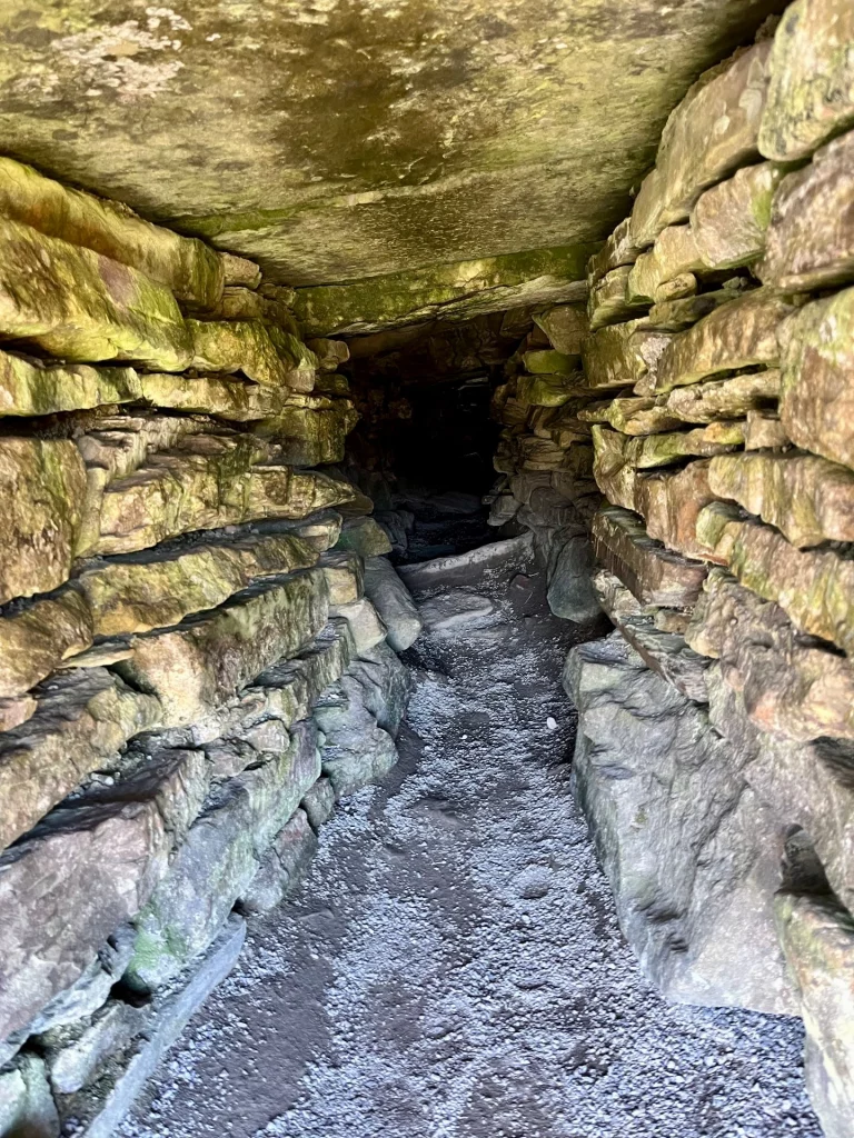 Nahaufnahme eines sehr engen, niedrigen Ganges im Inneren des Cairns mit massiven Steinwänden und einer flachen Steindecke.