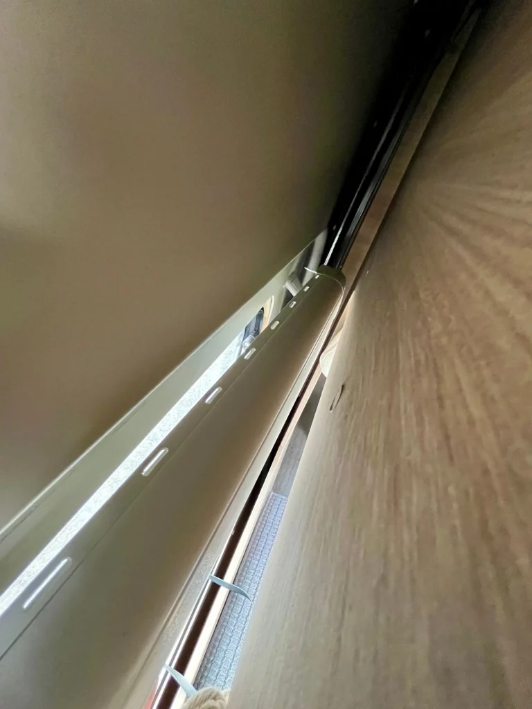 Perspektivische Ansicht von oben in den Zwischenraum eines gelösten Fensterrahmens. Man sieht die Rückseite des Kunststoffrahmens und die dahinterliegende Wandverkleidung.