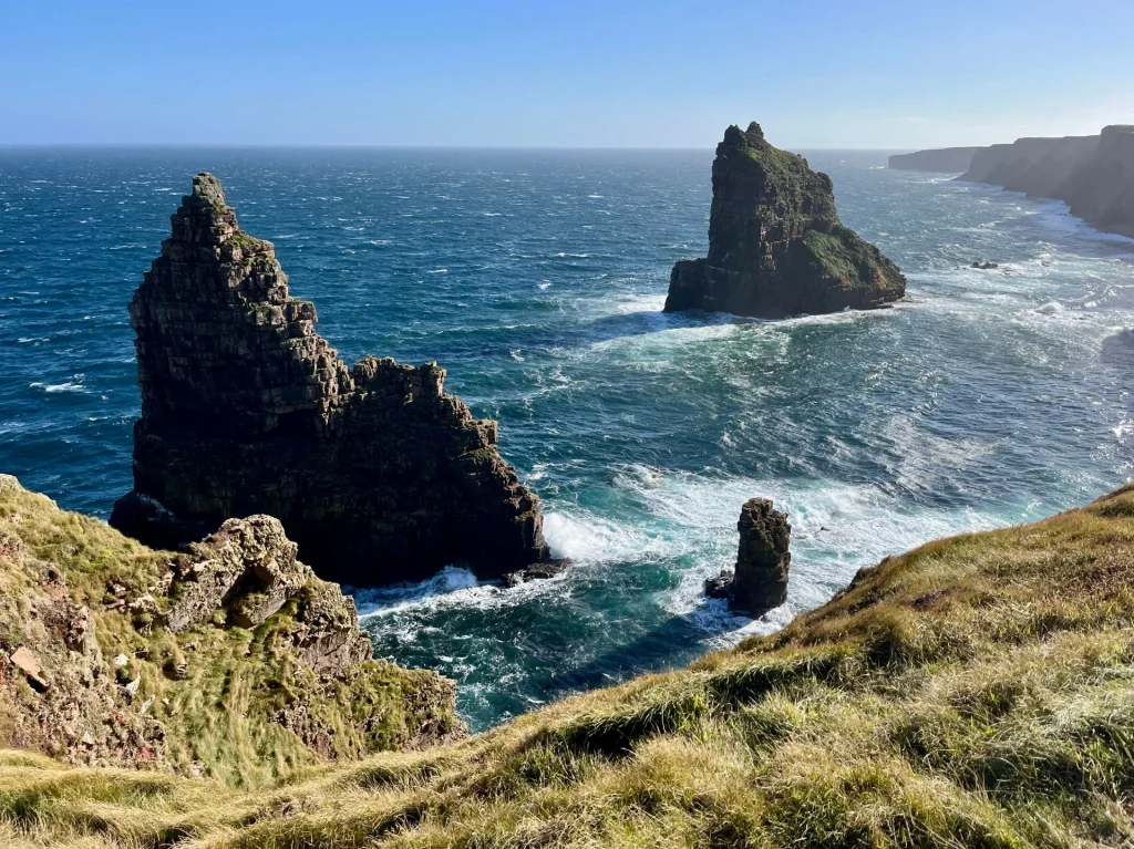 Spektakuläre, spitze Felsnadeln (Sea Stacks) im tobenden Atlantik vor der steilen Küstenlinie von Caithness.