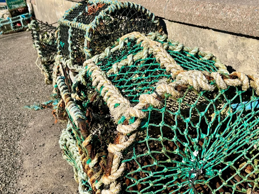 Nahaufnahme von traditionellen, mit grünen Netzen bespannten Hummerkörben und Fischreusen, die am Hafenrand auf dem Boden liegen.