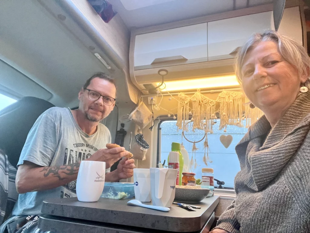 Ein Paar beim gemütlichen Frühstück am Tisch im Inneren ihres ausgebauten Kastenwagens während eines Schottland-Roadtrips.