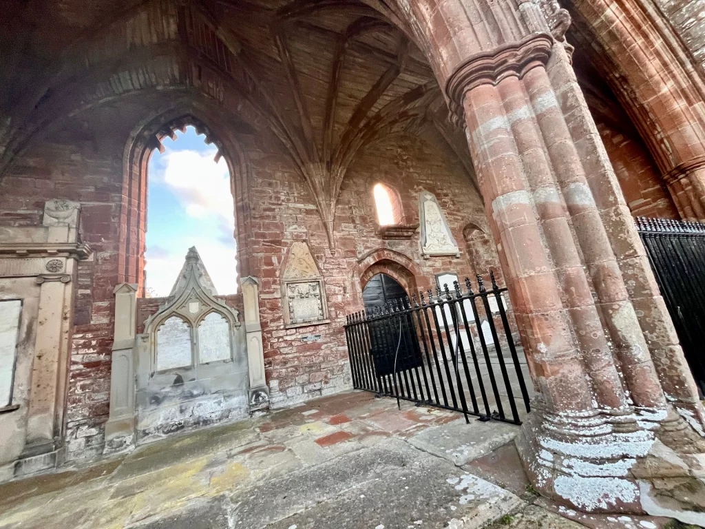 Perspektivische Innenansicht der Kathedralruine mit massiven Steinsäulen und gusseisernen Schutzgittern vor den Grabmälern.