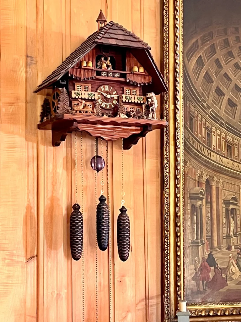 Eine detailreiche, hölzerne Kuckucksuhr im Schwarzwald-Stil mit geschnitzten Figuren und drei zapfenförmigen Gewichten an einer Holzwand.