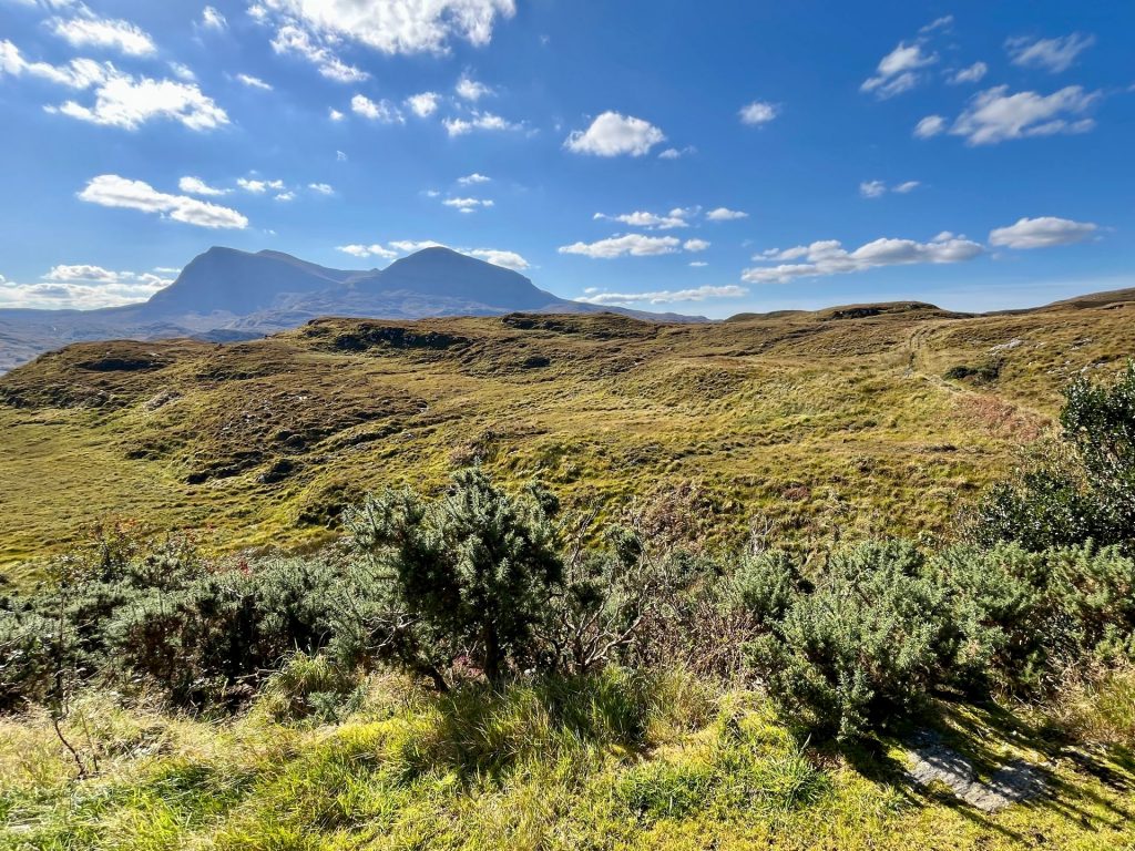 Spektakuläre Aussicht auf zwei fast perfekt symmetrische, pyramidenförmige Berge, die hinter einer ruhigen Wasserfläche aus der herbstlichen Highland-Landschaft ragen.