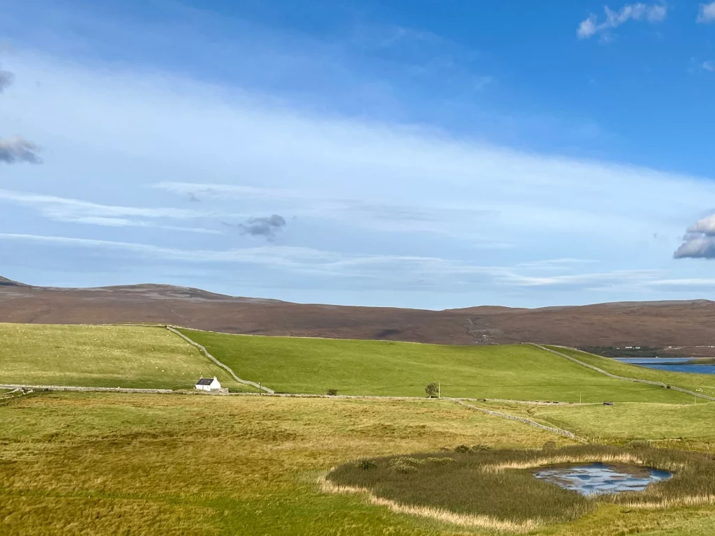 Typisch schottische Highland-Landschaft mit grünen Feldern, Steinmauern und einem einsamen weißen Cottage unter einem weiten Himmel am Loch Eriboll.