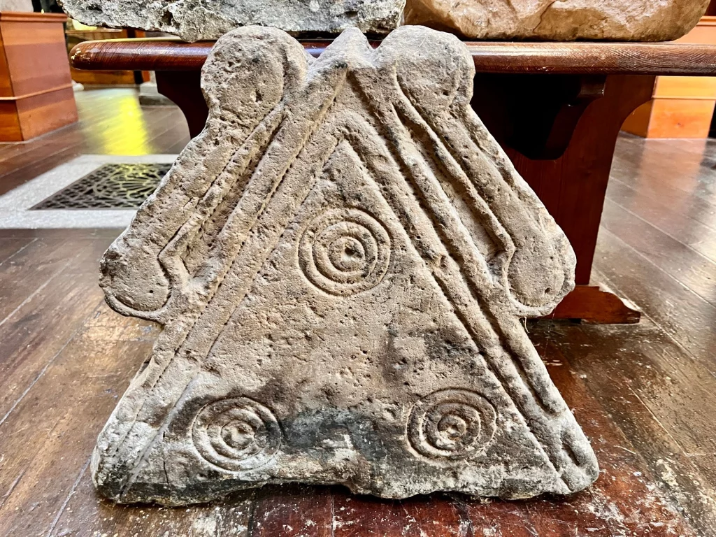 Ein dreieckiger piktischer Stein mit drei eingravierten konzentrischen Spiralen und tiefen Zierrillen.