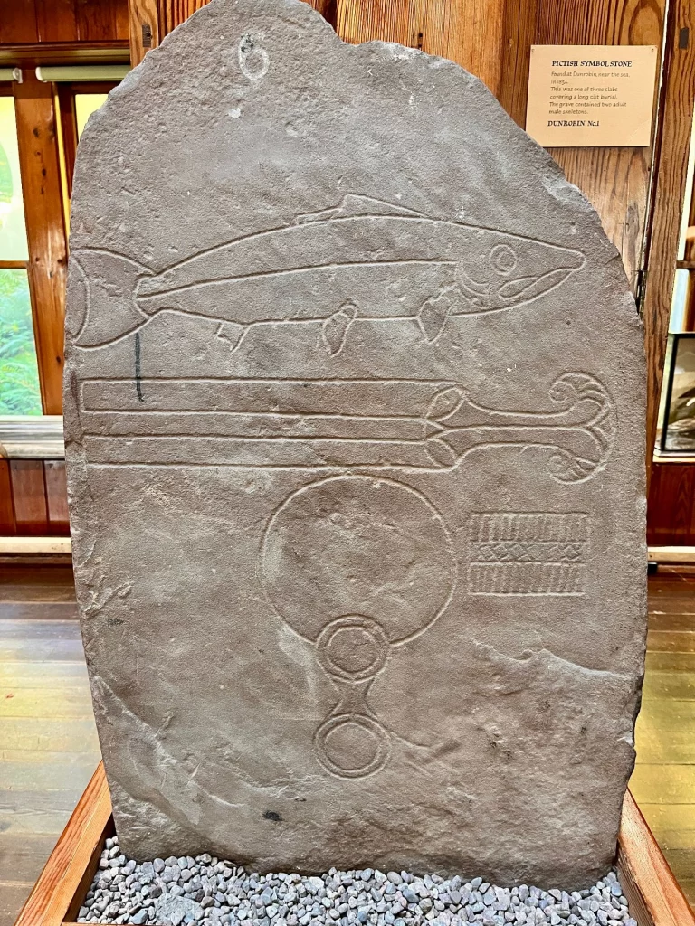 Aufrechter Sandstein mit den piktischen Symbolen Lachs, Doppelkamm und einem runden Handspiegel.