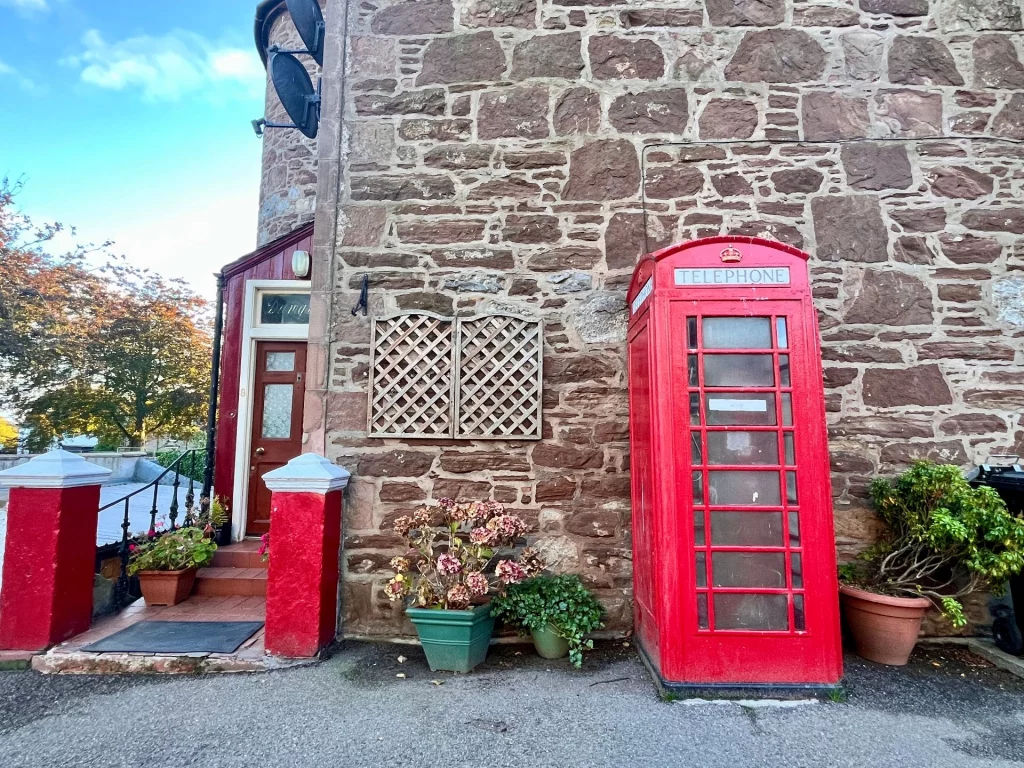 Eine klassische britische rote Telefonzelle vor einer rustikalen schottischen Natursteinwand in Tain.