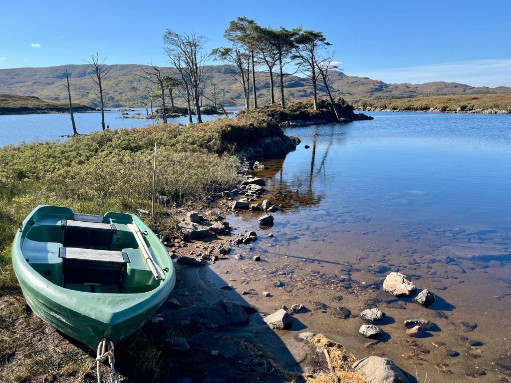 Vorderansicht eines hellgrauen Knaus BoxLife Wohnmobils, das auf einem Schotterparkplatz vor einer schottischen Seenlandschaft parkt.