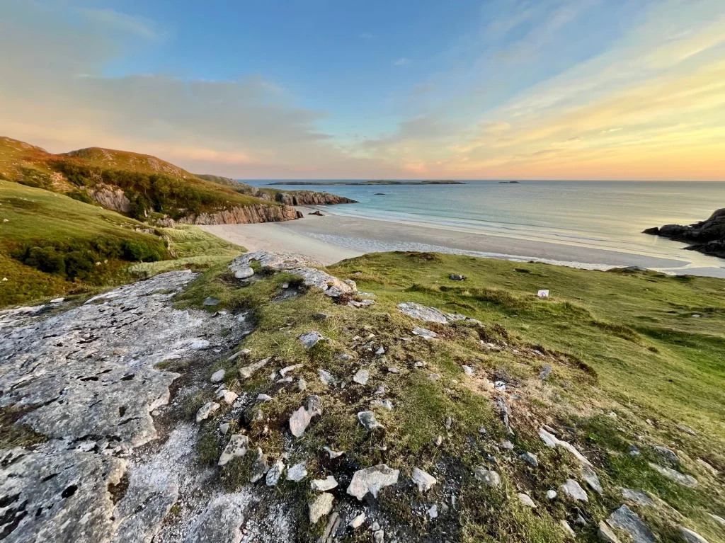 Weite Sicht von den Klippen auf den hellen Sandstrand der Sango Bay bei Durness im sanften Morgenlicht, mit Blick auf den ruhigen Nordatlantik und die schottische Küstenlandschaft.