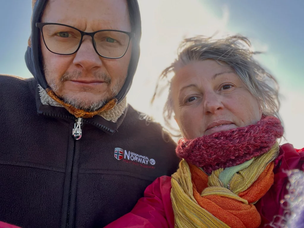 Ein lächelndes Paar in windfester Kleidung (Karin und Ingo) bei starkem Wind während ihres Schottland-Roadtrips.