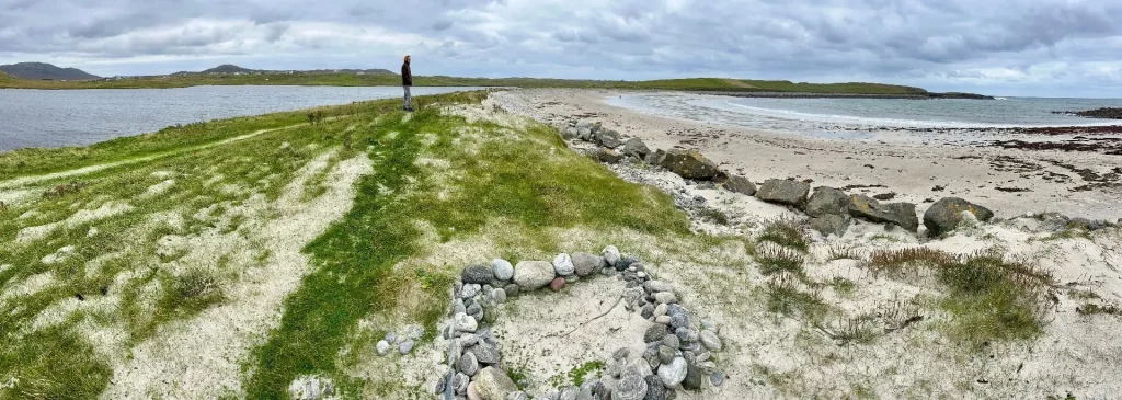 Weitwinkelaufnahme einer schmalen, flachen Landbrücke aus Sand und Steinen, die zwei Wasserflächen voneinander trennt, mit einer Person in der Ferne als Größenvergleich.