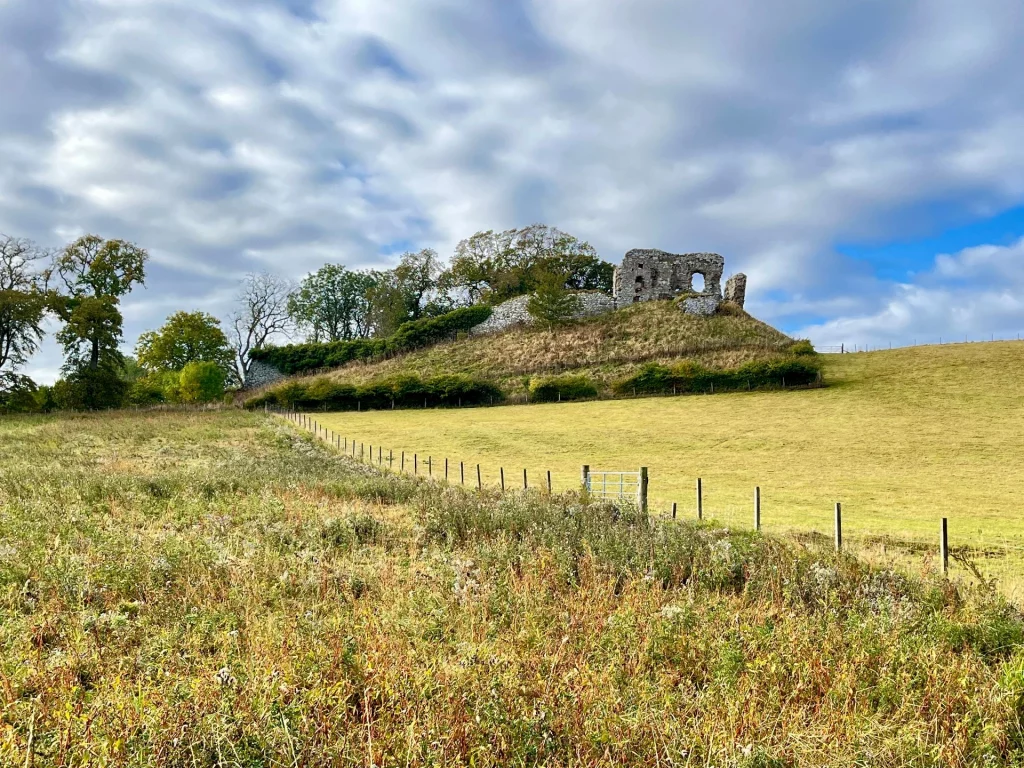 Ruine von Skelbo Castle auf einem grünen Hügel unter bewölktem Himmel in Sutherland, Schottland.