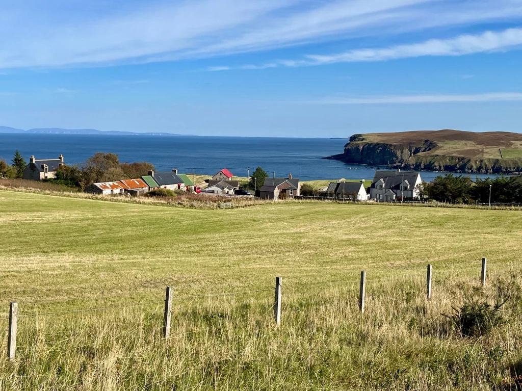 Eine weite Wiese mit Blick auf eine kleine Küstensiedlung am tiefblauen Atlantik.