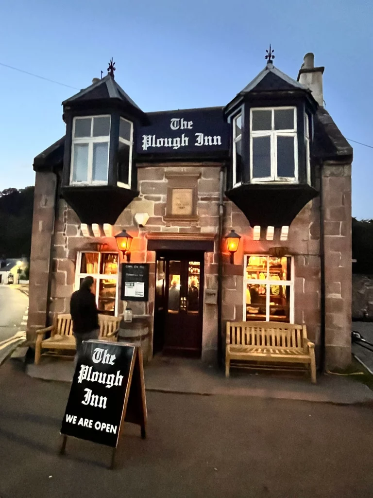 Die beleuchtete Außenfassade des Pubs „The Plough Inn“ in der Dämmerung. Das Gebäude aus Naturstein hat zwei markante Erkerfenster im Obergeschoss und ein Schild vor der Tür, das besagt, dass geöffnet ist.

Bild 3: Guinness-Tukan an der Bar