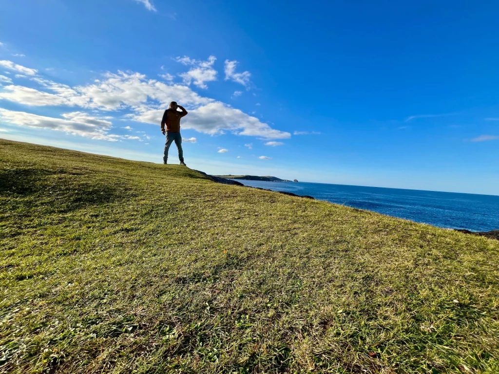 Ein Mann steht als Silhouette auf einer Anhöhe und blickt mit der Hand an der Stirn über den weiten, tiefblauen Atlantik.