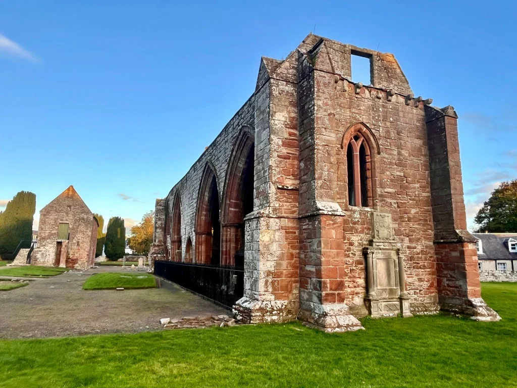 Außenansicht der hohen, fensterlosen Westwand des Südgangs der Kathedrale auf einer gepflegten Rasenfläche.