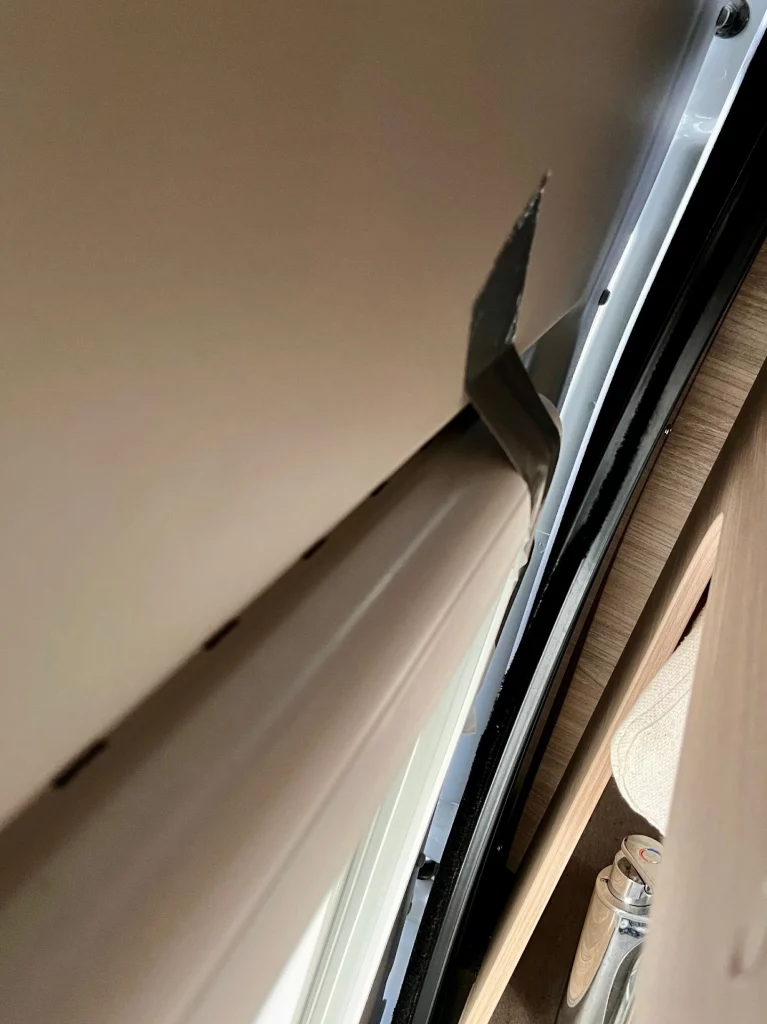 Nahaufnahme eines weißen Fensterrahmens im Innenraum eines Wohnmobils, der sich von der Wand gelöst hat. Ein Streifen schwarzes Panzerband hängt lose am Rahmen.