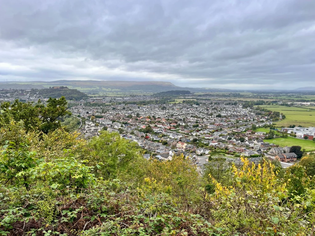 Panorama-Ausblick vom Abbey Craig auf die Stadt Stirling und die umliegende Hügellandschaft unter Wolken.