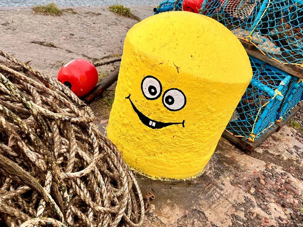 Nahaufnahme eines leuchtend gelb bemalten Pollers mit einem aufgemalten Smiley-Gesicht und Zähnen.