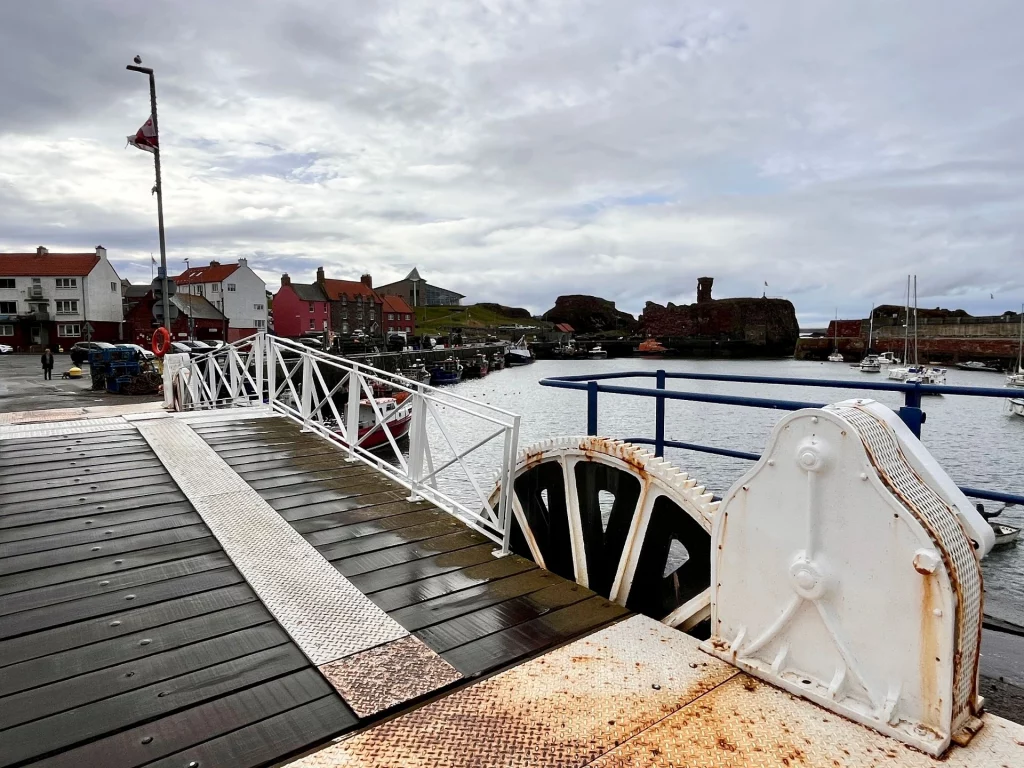 Blick über eine weiße Klappbrücke im Hafen von Dunbar mit großen mechanischen Zahnrädern im Vordergrund.
