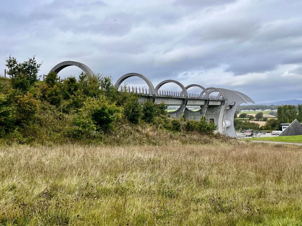 Weitwinkelaufnahme des Falkirk Wheels und des Aquädukts, eingebettet in die grüne, hügelige Landschaft Schottlands.