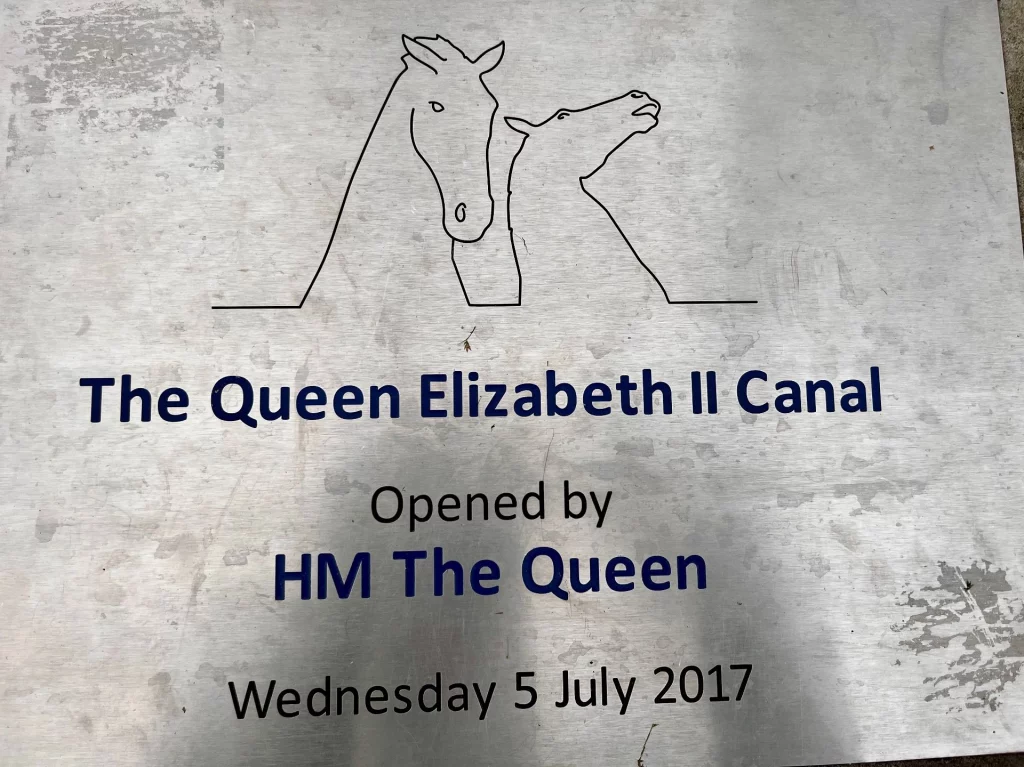 Eine silberne Gedenktafel mit einer Strichzeichnung der Kelpies-Skulpturen. Der Text besagt: "The Queen Elizabeth II Canal, Opened by HM The Queen, Wednesday 5 July 2017".