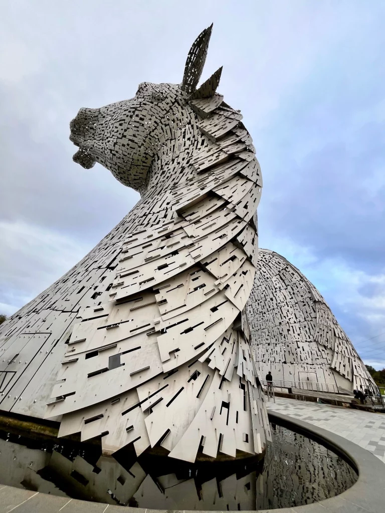 Nahaufnahme der Kelpie-Skulptur von unten, die die überlappenden Edelstahlplatten und die filigrane Konstruktion der Pferdemähne zeigt.