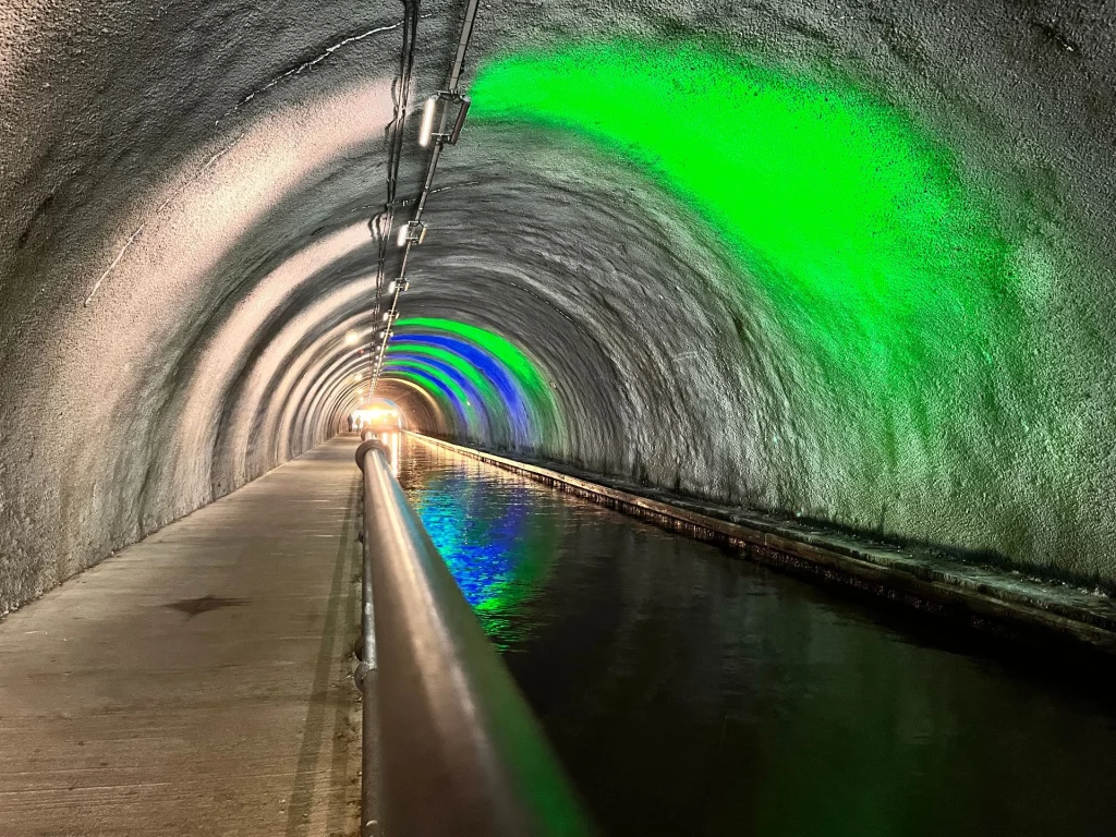 Innenansicht des Roughcastle Tunnels am Falkirk Wheel mit Spiegelungen von blauem und grünem Licht auf der Wasseroberfläche des Kanals.