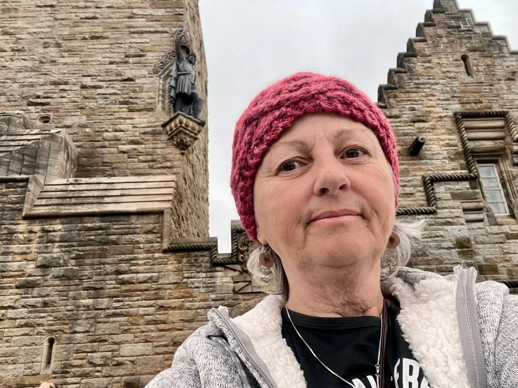 Eine Frau mit roter Strickmütze macht ein Selfie vor dem historischen Mauerwerk des Wallace Monument.