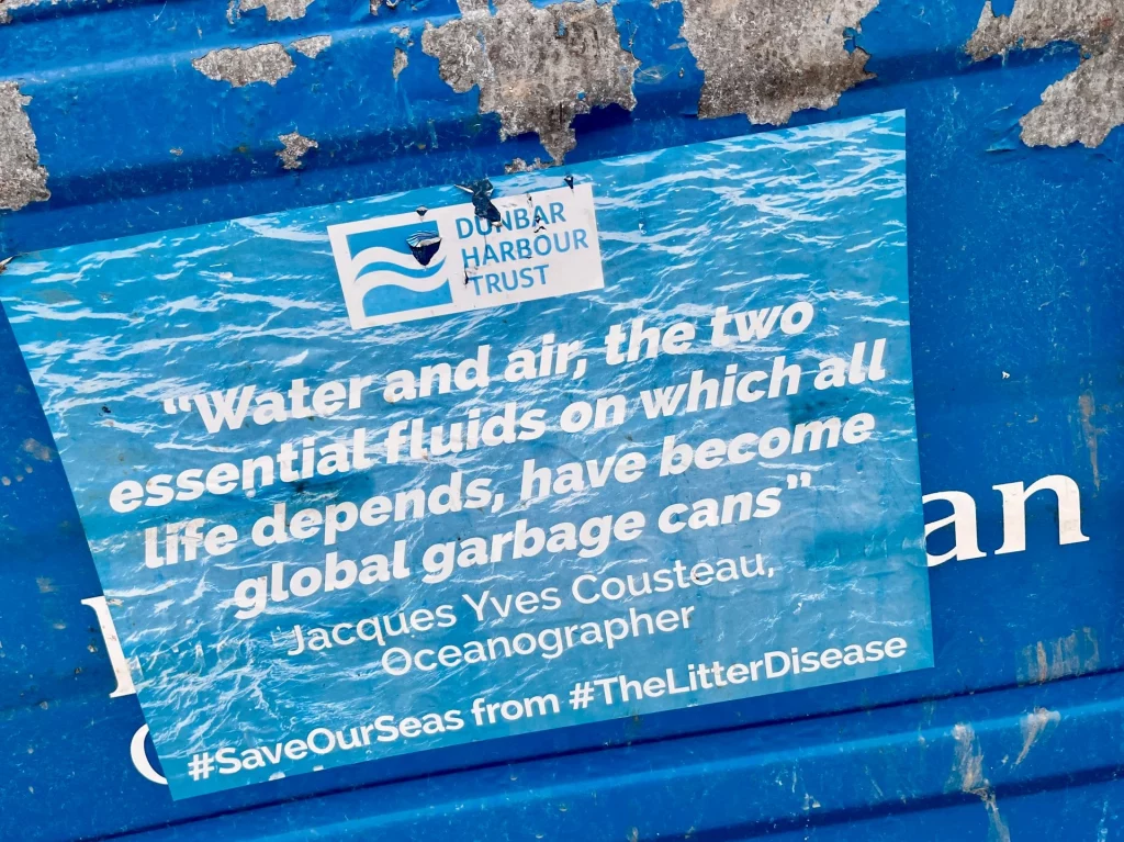 Ein blauer Aufkleber des Dunbar Harbour Trust mit einem Zitat von Jacques Cousteau über den Schutz der Meere vor Müll.