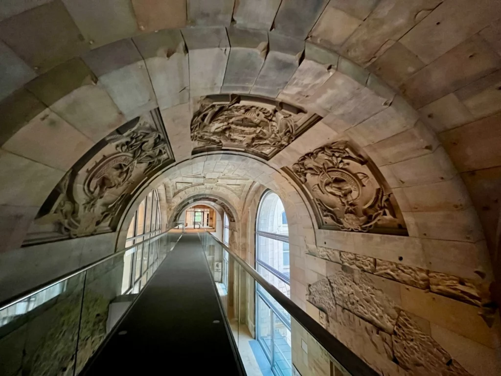Architekturgeschichte zum Anfassen: Dieser Gang (Richtung Toiletten) im Reichstag zeigt eindrucksvoll die Spuren der Zeit. Während man auf modernen Glaswegen wandelt, blickt man direkt auf die detailreichen Steinmetzarbeiten an den Deckenwölbungen. Besonders faszinierend ist der Kontrast zwischen dem rauen, geschichtsträchtigen Naturstein und der kühlen Transparenz der heutigen Architektur.