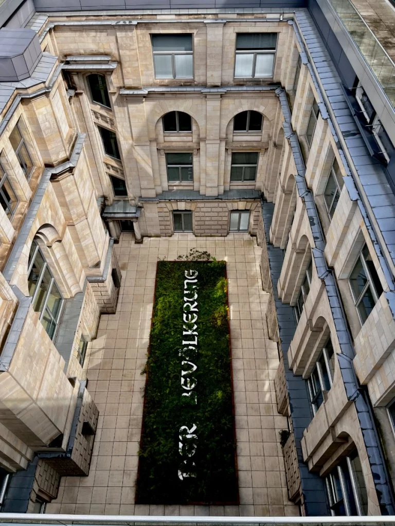 Ein starkes Symbol im Herzen des Parlaments: Das Kunstprojekt von Hans Haacke im nördlichen Lichthof. Der leuchtende Schriftzug ‚DER BEVÖLKERUNG‘ bildet das Pendant zur berühmten Inschrift ‚Dem Deutschen Volke‘ am Außenportal. Besonders spannend: Die Erde im Beet stammt aus den Wahlkreisen der Abgeordneten und die Pflanzen dürfen hier völlig wild und ungestört wachsen – ein lebendiges Bild für die Vielfalt der Gesellschaft.