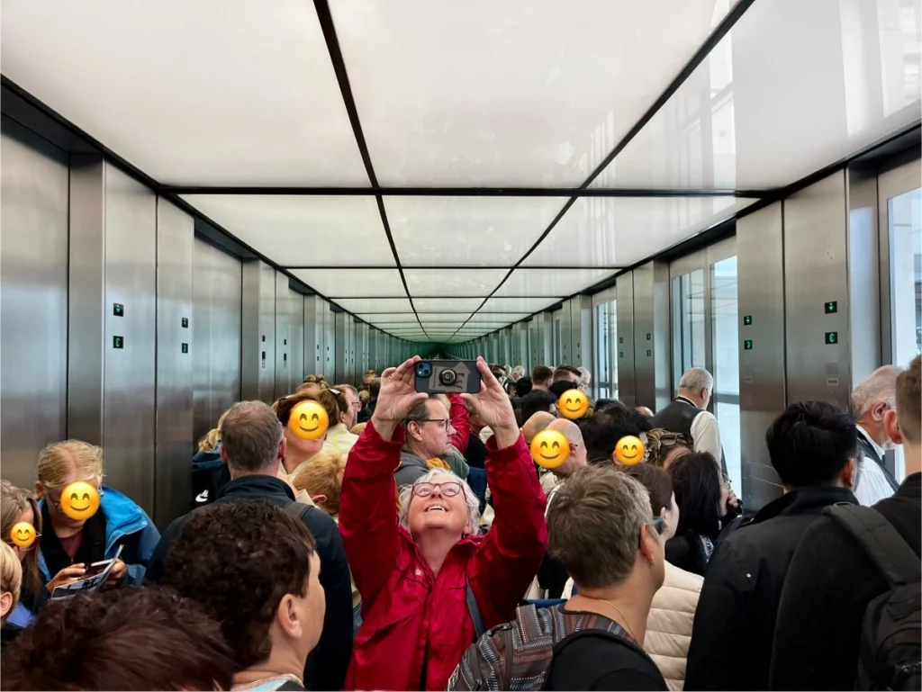 Spiegelspiel im Fahrstuhl: Während der Fahrt nach oben nutzen wir die verspiegelten Wände für ein schnelles Selfie. Ich (Karin) halte das Handy hoch, um die futuristische Beleuchtung einzufangen, und rahme dabei Ingo zwischen meinen Armen ein. Das Bild vermittelt perfekt die geschäftige, aber freudige Stimmung der Besuchergruppe auf dem Weg zur Dachterrasse.