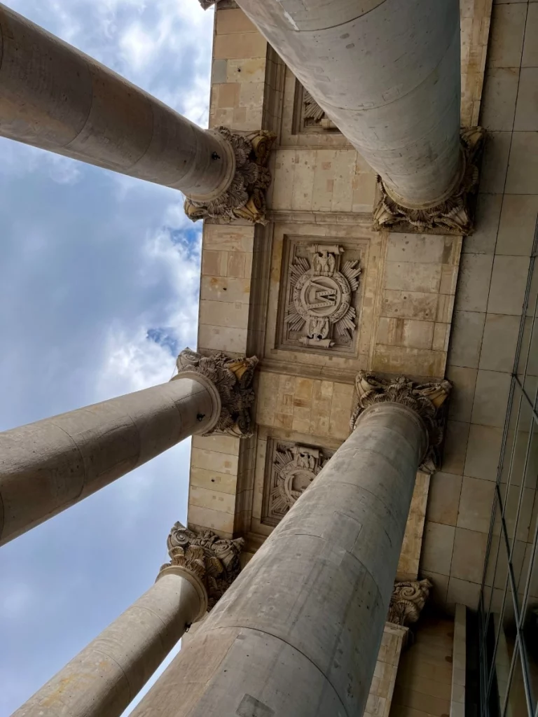 Ein Blick, der die Ehrfurcht gebietende Größe des Reichstags einfängt: Die gewaltigen Säulen ragen wie steinerne Wächter empor und rahmen die kunstvollen Reliefs an der Decke ein. Diese Perspektive macht die Verbindung von Macht, Geschichte und meisterhafter Steinmetzkunst direkt greifbar, bevor man das moderne Innere des Parlaments betritt.