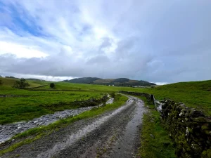 Ein matschiger, wassergefüllter Feldweg in den schottischen Highlands unter einem dramatisch grauen Regenwolkenhimmel.