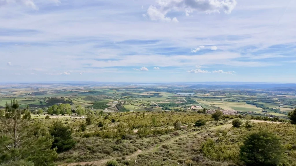 Weite Panorama-Aussicht von der Burg Castillo de Loarre auf die grüne und landwirtschaftlich geprägte Ebene Hoya de Huesca in Aragonien, Spanien, unter einem leicht bewölkten blauen Sommerhimmel.