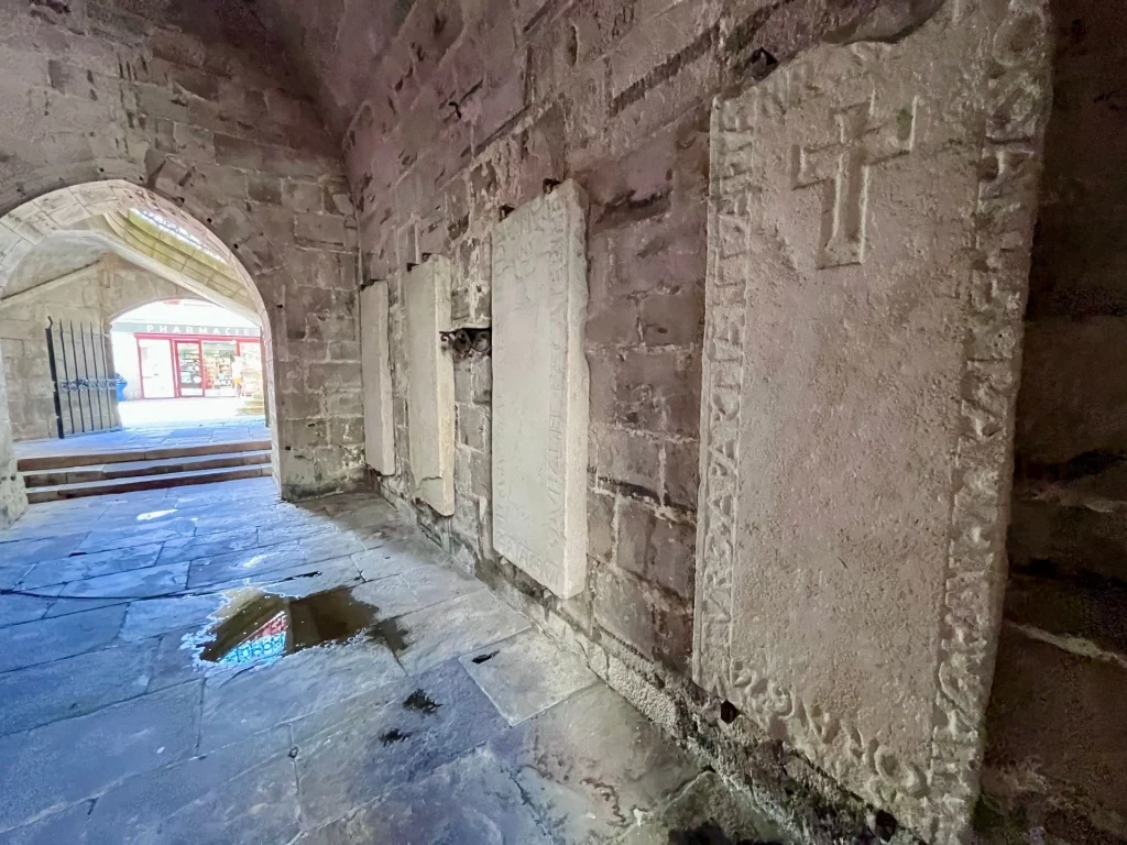 Historischer, steinerner Klostergang mit gotischen Gewölben und alten, aufrecht an der Wand angebrachten Grabplatten mit eingemeißelten Kreuzen.