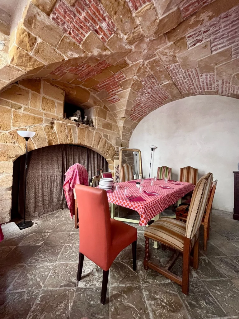 Rustikaler Gastraum in Bayonne unter einem historischen Steingewölbe mit roten Backstein-Akzenten, ausgestattet mit einem großen, festlich gedeckten Holztisch und bunten Stühlen.