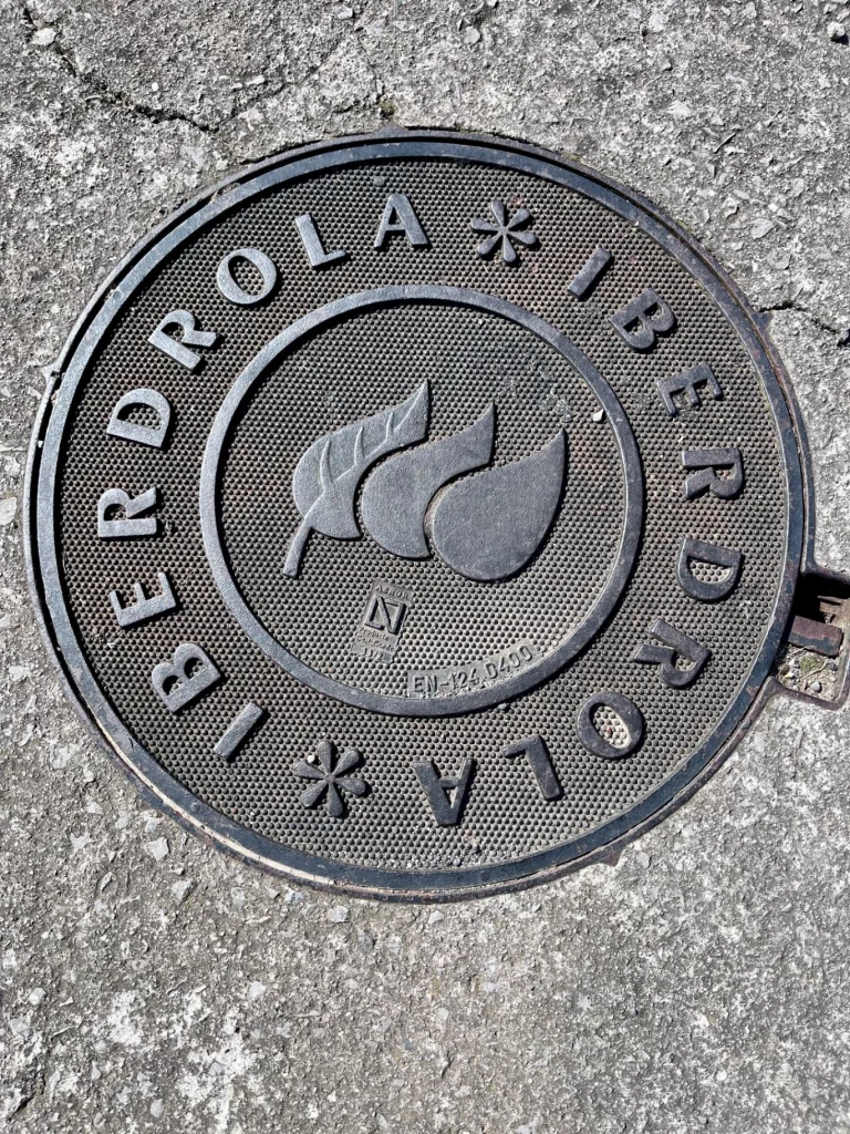 Nahaufnahme eines runden, gusseisernen Gullydeckels mit dem Logo und der Aufschrift des Energieunternehmens Iberdrola.