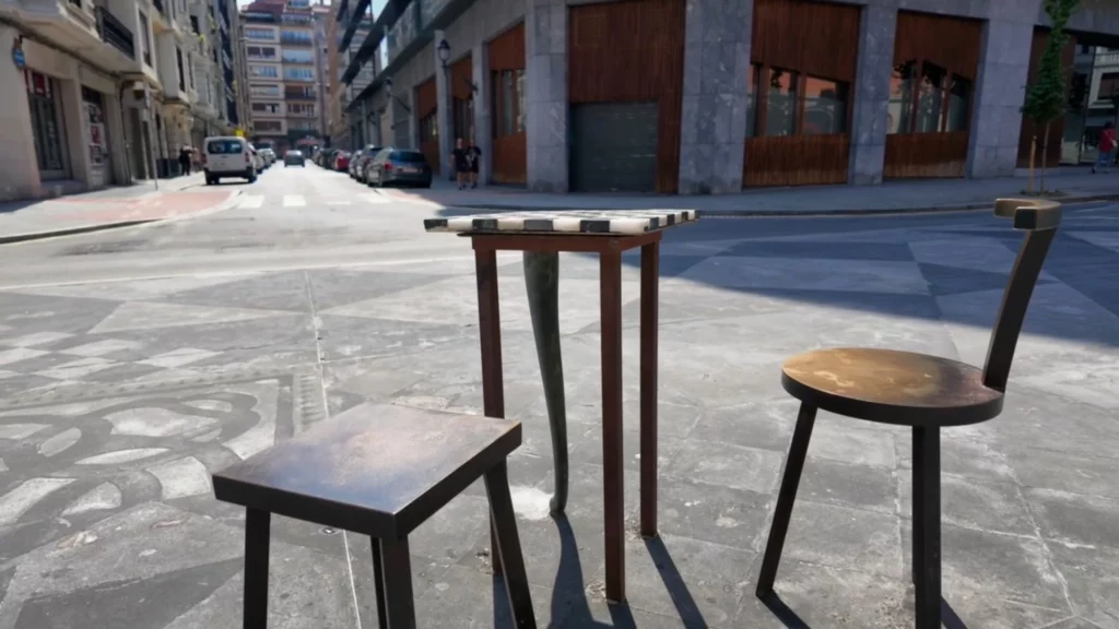 Eine Street-Art-Skulptur bestehend aus einem kleinen Tisch mit Schachbrettmuster und zwei Stühlen mitten auf einem gepflasterten Platz.