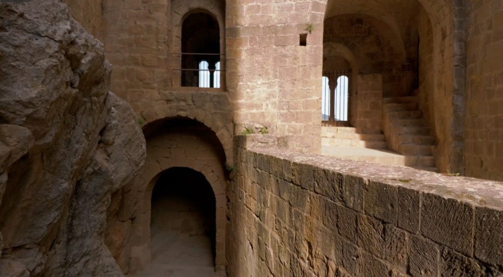 Massive, helle Sandsteinmauern, Torbögen und eine Steintreppe im Castillo de Loarre, direkt an den natürlichen Felsen gebaut.