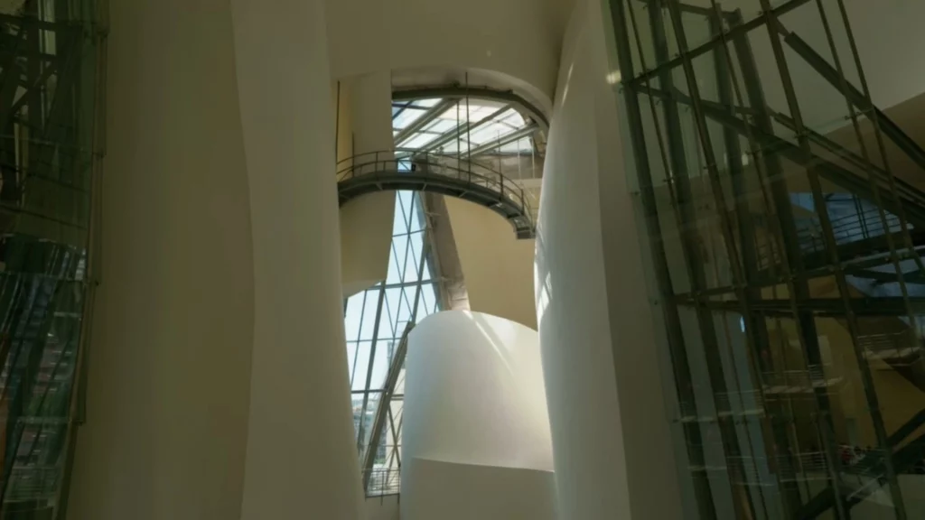 Eine weite Innenansicht des Atriums im Guggenheim-Museum mit riesigen, geschwungenen weißen Säulen und großen Fensterfronten, durch die das Tageslicht fällt.