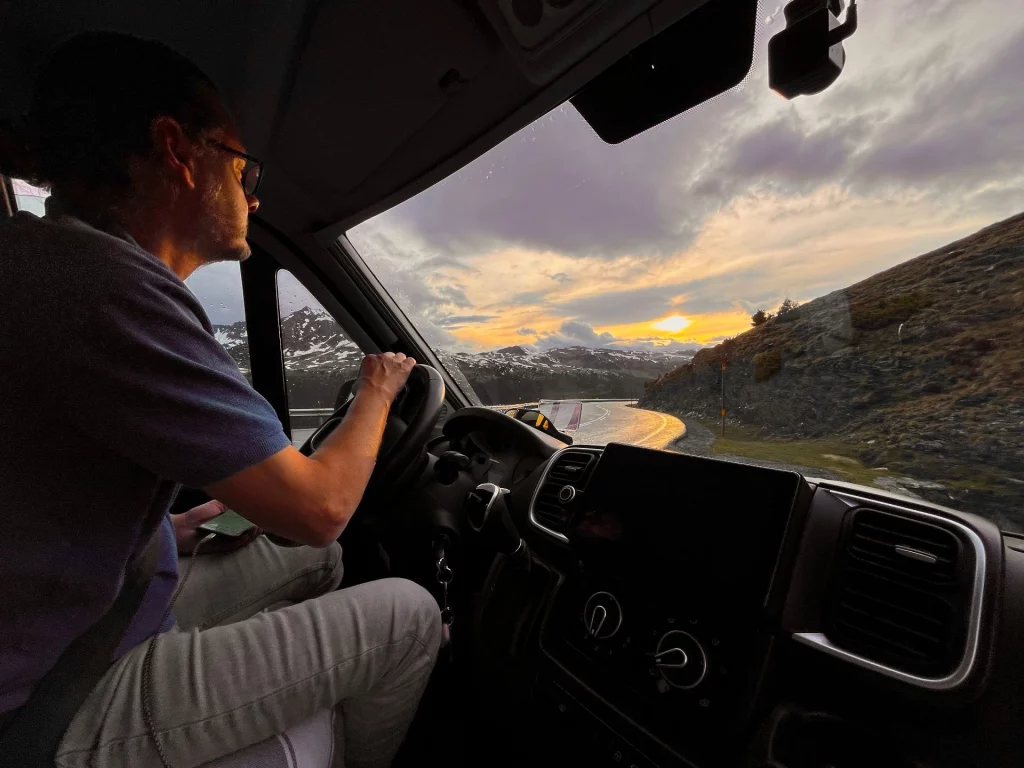 Ingo im Profil am Lenkrad des Wohnmobils beim Fahren während eines goldenen Sonnenuntergangs über den Bergen.