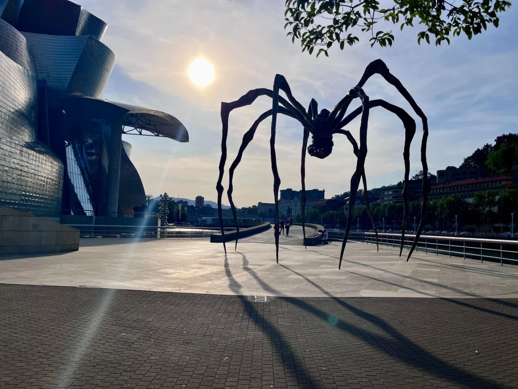 Die riesige Bronzeskulptur Maman von Louise Bourgeois im Gegenlicht der tiefstehenden Sonne an der Strandpromenade neben dem Guggenheim-Museum in Bilbao.