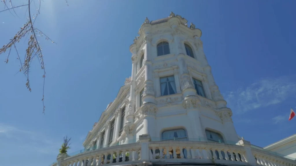 Froschperspektive auf die weiße, prunkvolle Fassade und den markanten Eckturm des Palacio de la Magdalena in Santander unter strahlend blauem Himmel.